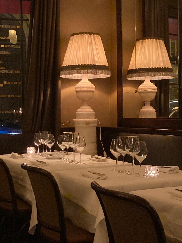 tables dressées dans le restaurant bistrot gastronomique "Les Jalles", rue des capucines à Paris. La lumière est tamisée. Rideau, miroirs, photophore, et une très belle lampe avec abat-jour crème.